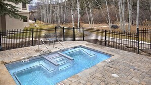 Una piscina rectangular al aire libre con una cerca de metal negro, rodeada por una zona pavimentada con losas de piedra.