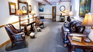 Una habitación con un sofá de cuero, dos sillones, una mesa de centro de madera y una mesa de comedor con lámparas. Hay cuadros en las paredes y un cuadro sobre el sofá.