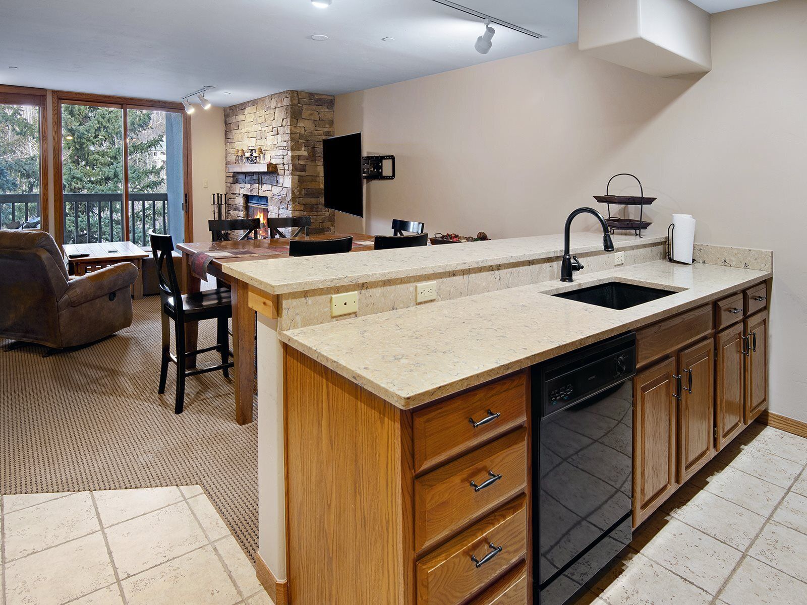 A modern kitchen with a large island, wooden cabinets, and a stone fireplace.