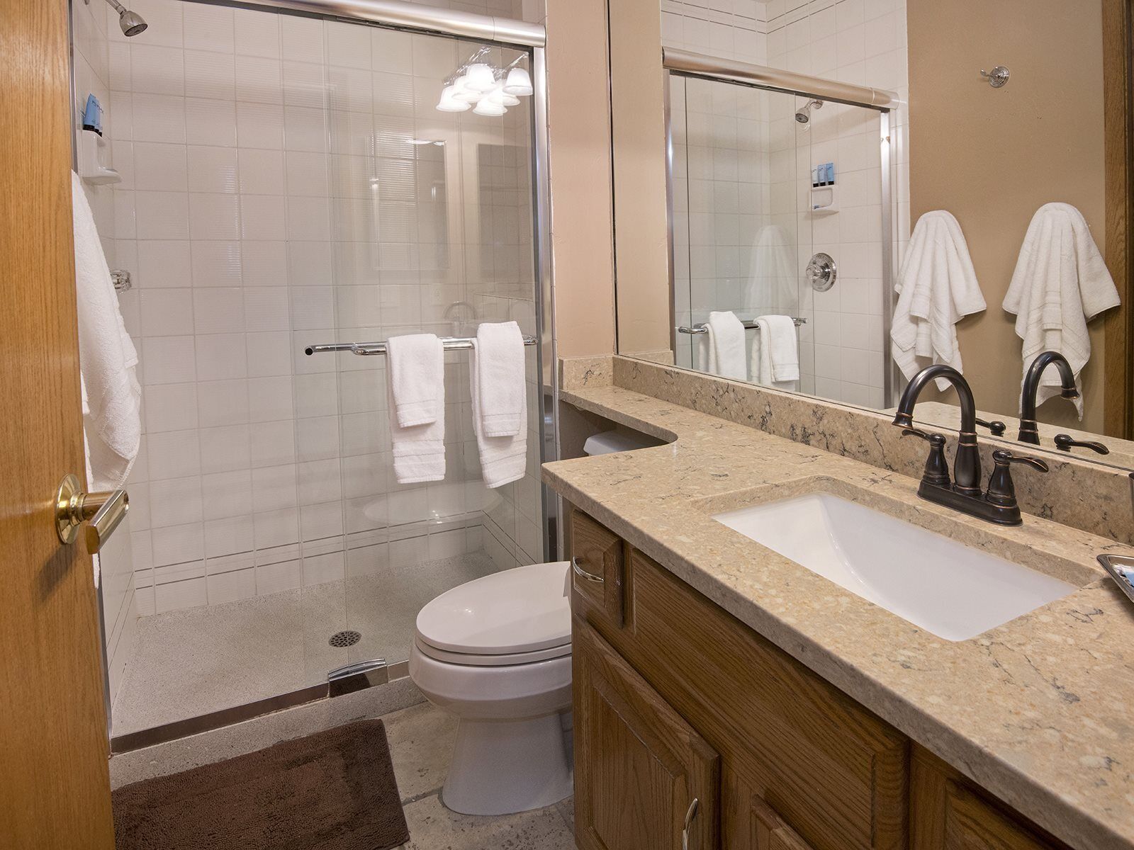 A modern bathroom with a glass shower enclosure, a white toilet, and a marble sink with a large mirror.