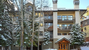Un edificio de varios pisos con balcones, una entrada cubierta de nieve y un entorno de estación de esquí.