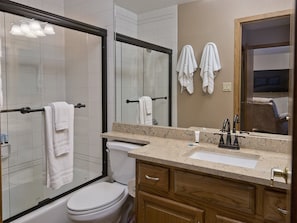 A bathroom with a glass shower enclosure, a toilet, a sink with a mirror, and wooden cabinets. - Beaver Creek Condo - Townsend 205 (Avon)
