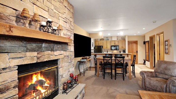 Una sala de estar con chimenea de piedra, un comedor y una cocina con armarios de madera y un televisor de pantalla plana.
