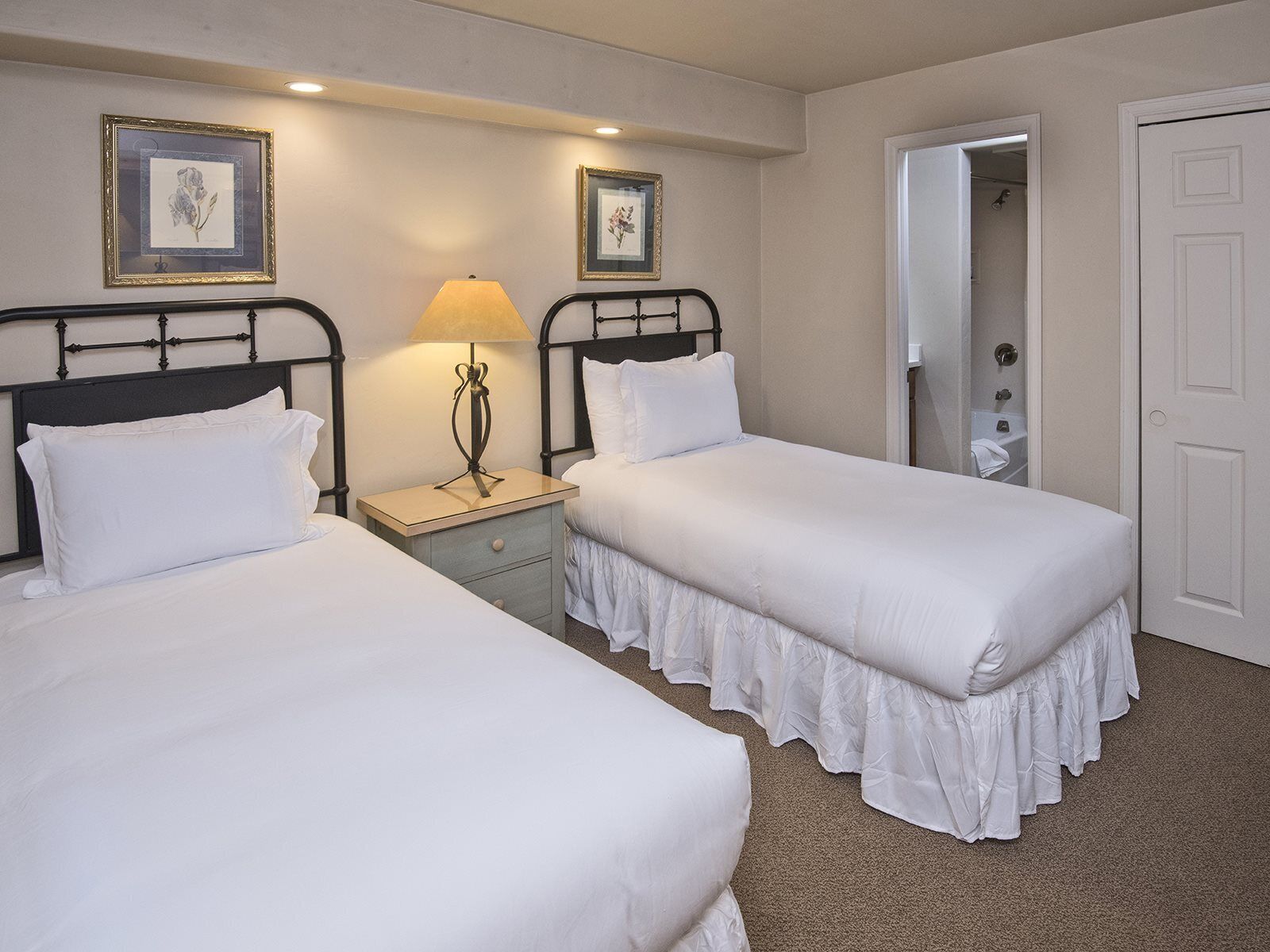 Ein Hotelzimmer mit zwei Einzelbetten, einem Nachttisch mit Lampe und einer Tür zu einem Badezimmer.