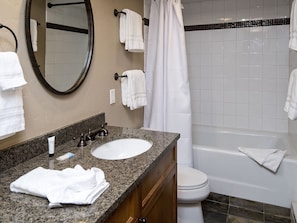 A bathroom with a granite countertop, white sink, and a toilet. There are multiple white towels hanging on hooks and a shower curtain. - Vantage Point Condo 201 (Vail)
