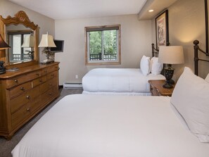 A bedroom with two beds, a dresser, a TV, and a window with a view of greenery. - Vantage Point Condo 201 (Vail)