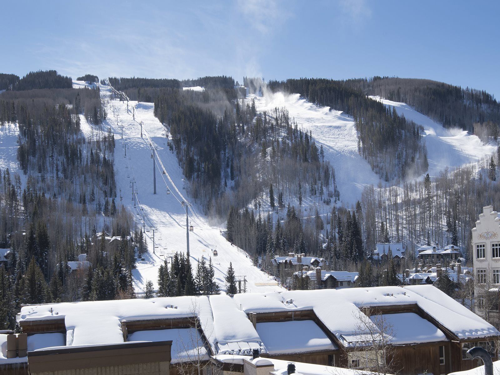 A snow-covered mountain with ski lifts, a town with wooden buildings, and a clear blue sky.
