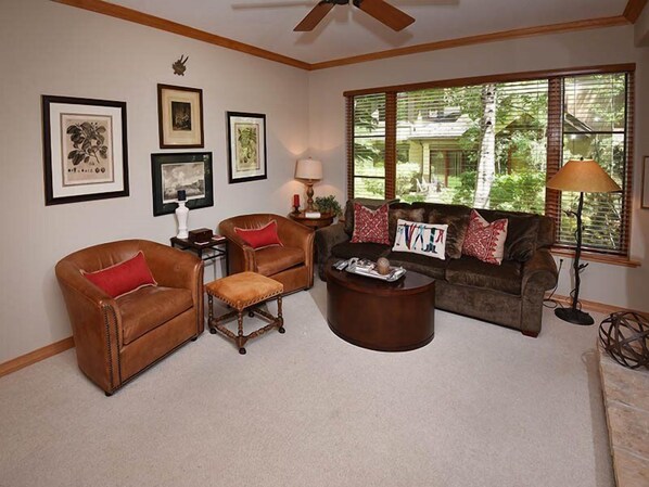 A living room with a brown leather sofa, two armchairs, a coffee table, and a large window with blinds.