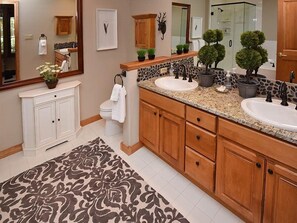 A spacious bathroom with two sinks, wooden cabinets, a large mirror, and a patterned rug.