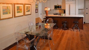 A modern kitchen with white cabinets, a central island with stools, and a dining area with a glass table and chairs. - Arrowhead Village Condo - 104 Seasons Lodge (Edwards)
