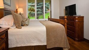 A bedroom with a bed, a dresser, a television, and a window with a view of trees. - Arrowhead Village Condo - 104 Seasons Lodge (Edwards)