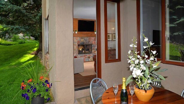 A patio with a wooden table set for two, a potted plant, and a bottle of champagne. - Arrowhead Village Condo - 104 Seasons Lodge (Edwards)