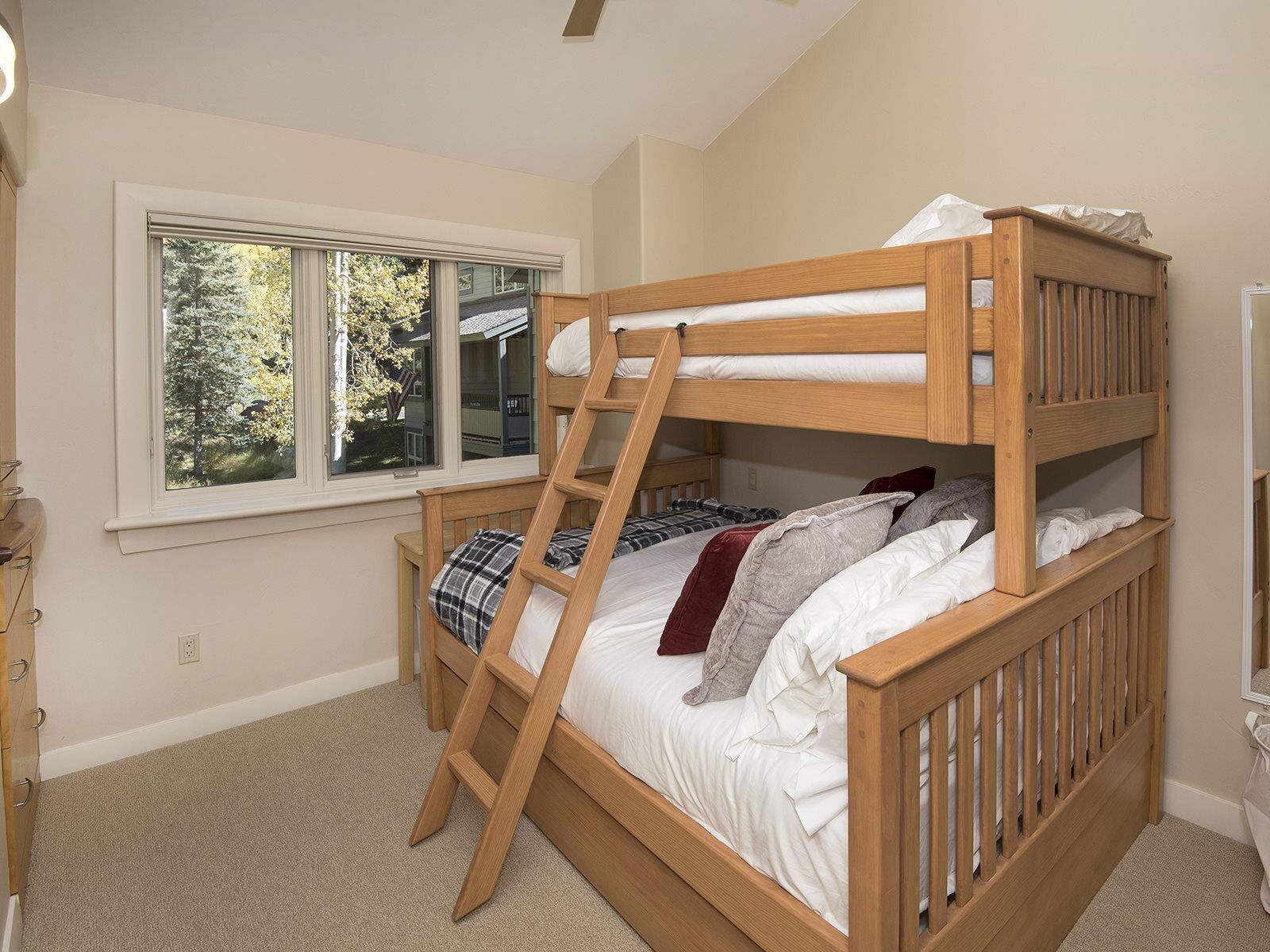 A bunk bed with a ladder, a window with a view of trees, and a dresser.
