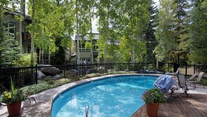 A swimming pool with a wooden deck, surrounded by a black fence and potted plants.