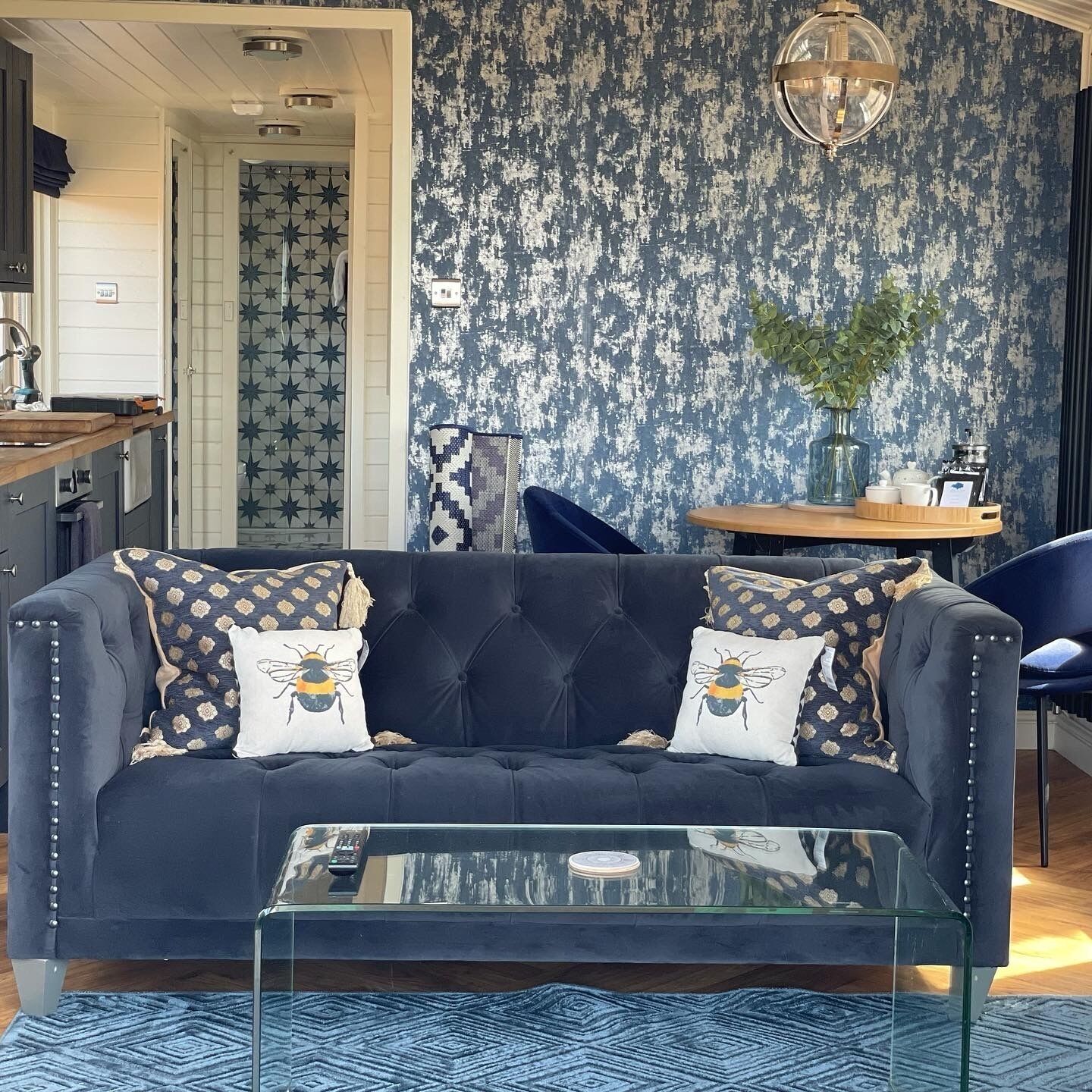 A living room with a dark blue sofa, two decorative pillows, a glass coffee table, and a patterned rug.