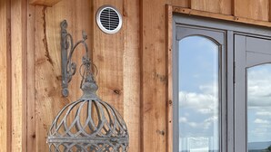 Pared exterior de madera con un farol metálico decorativo y una ventana.