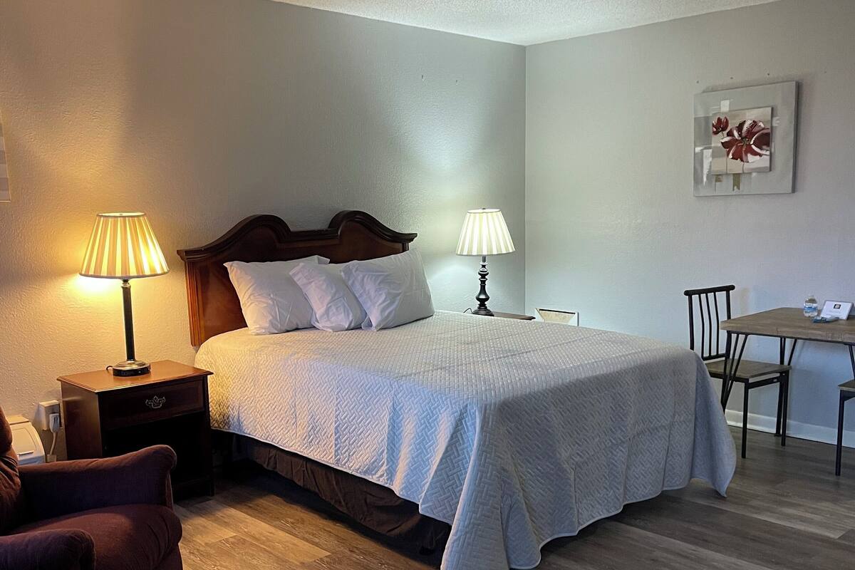 Quarto bem arrumado com uma cama, duas luminárias de mesa, uma cadeira de madeira e uma mesinha.