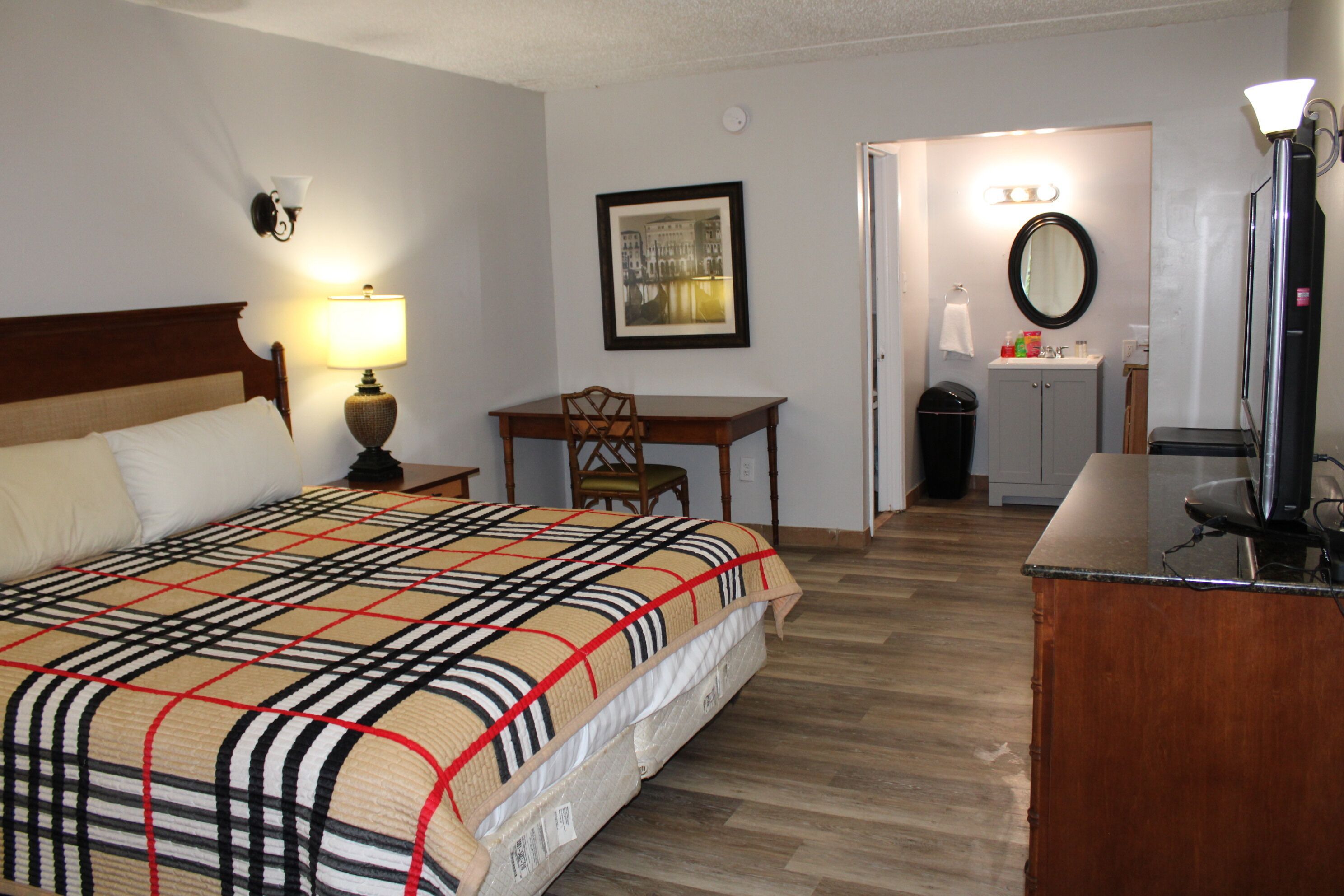 Habitación de hotel con cama, escritorio, silla, televisión y baño visible a través de una puerta abierta.