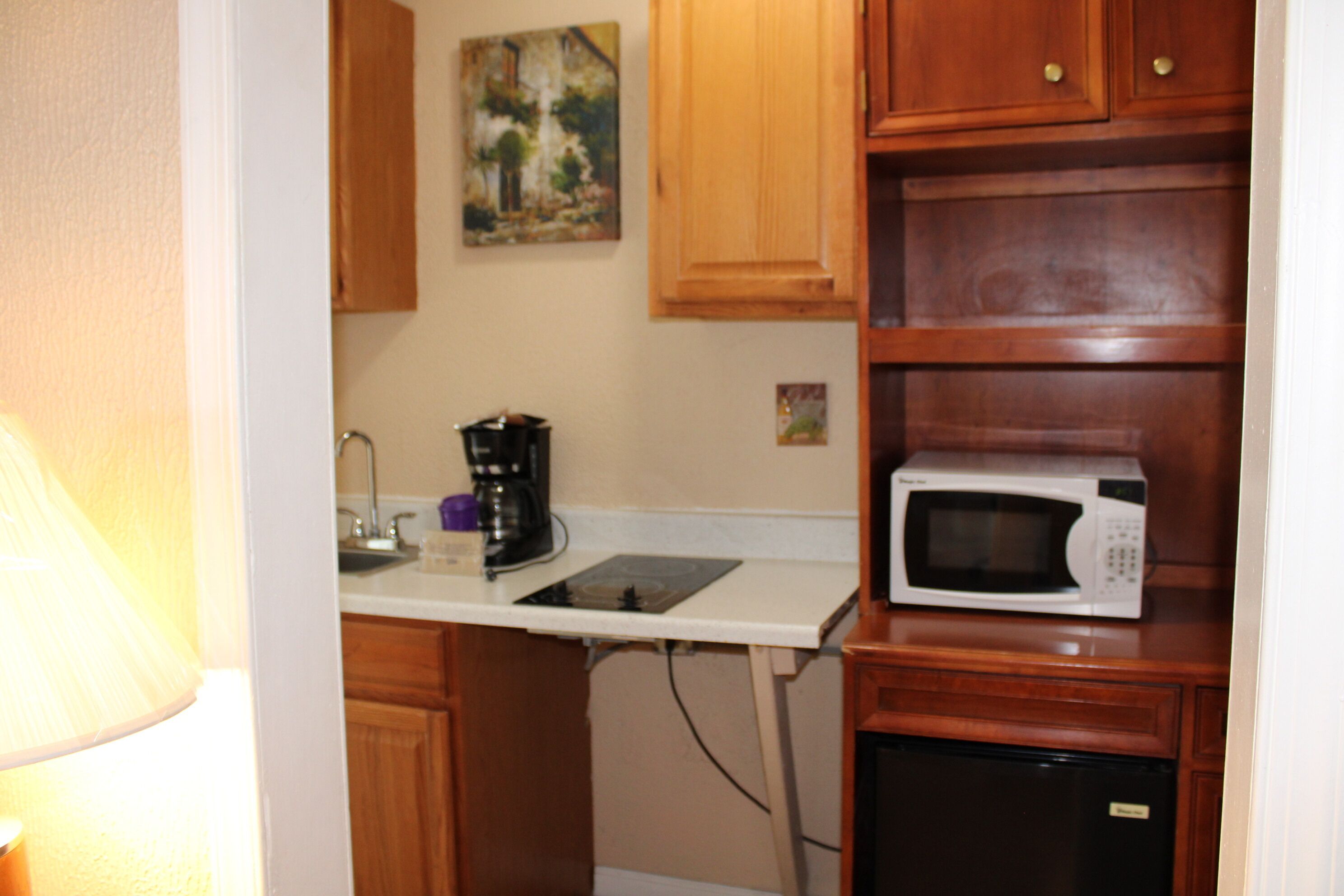 A compact kitchen with wooden cabinets, a microwave, a coffee maker, and a small refrigerator.