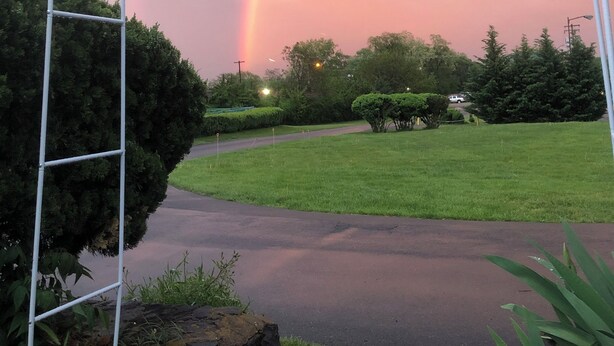 Ein Metallbogen in einem Park, im Hintergrund ein Regenbogen.