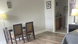 Ein Zimmer mit Esstisch und Stühlen, einem Bett sowie einer durchgehenden Tür erkennbaren Küchenzeile.