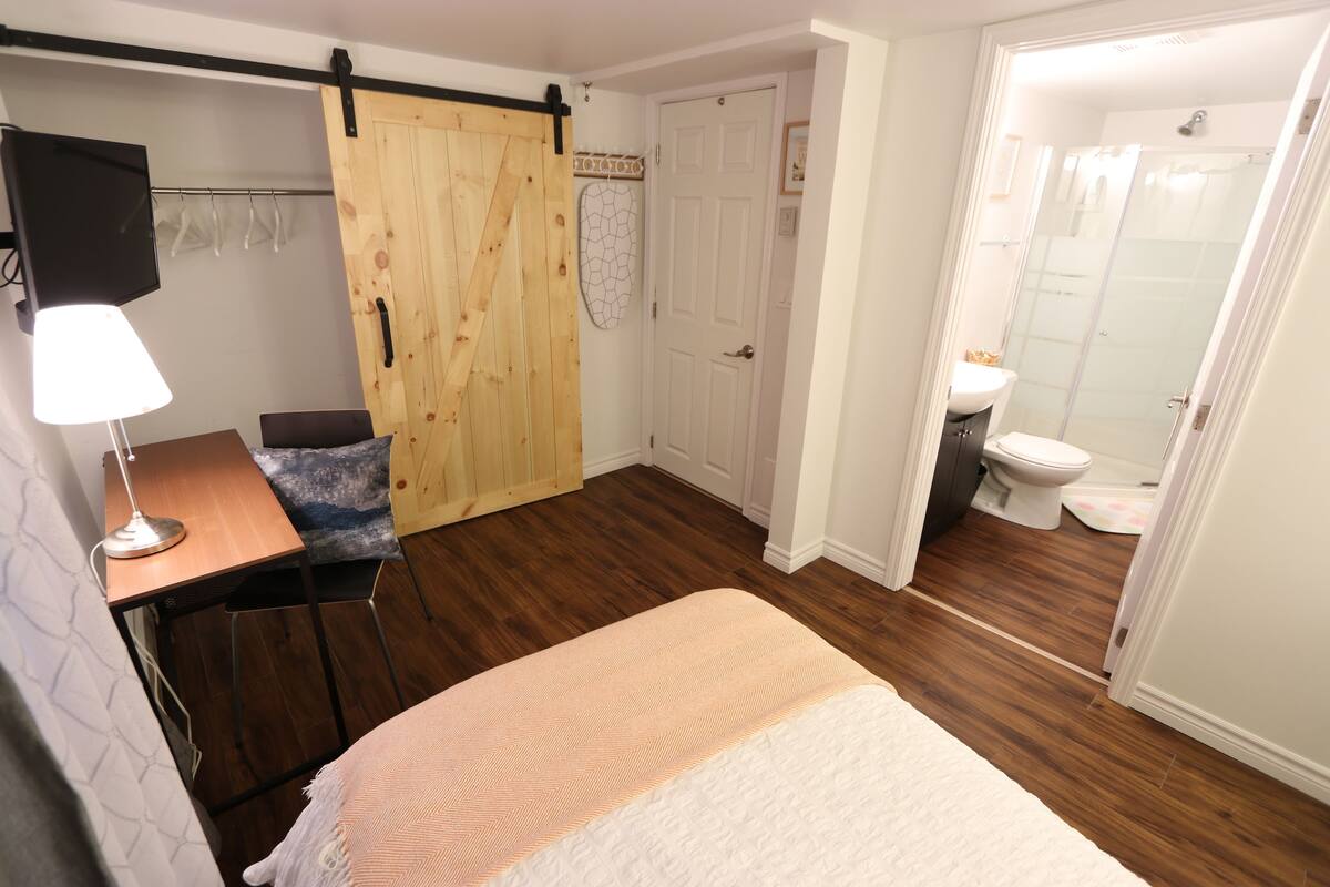 A bedroom with a bed, a desk with a lamp, a wardrobe, and a bathroom with a shower and toilet.