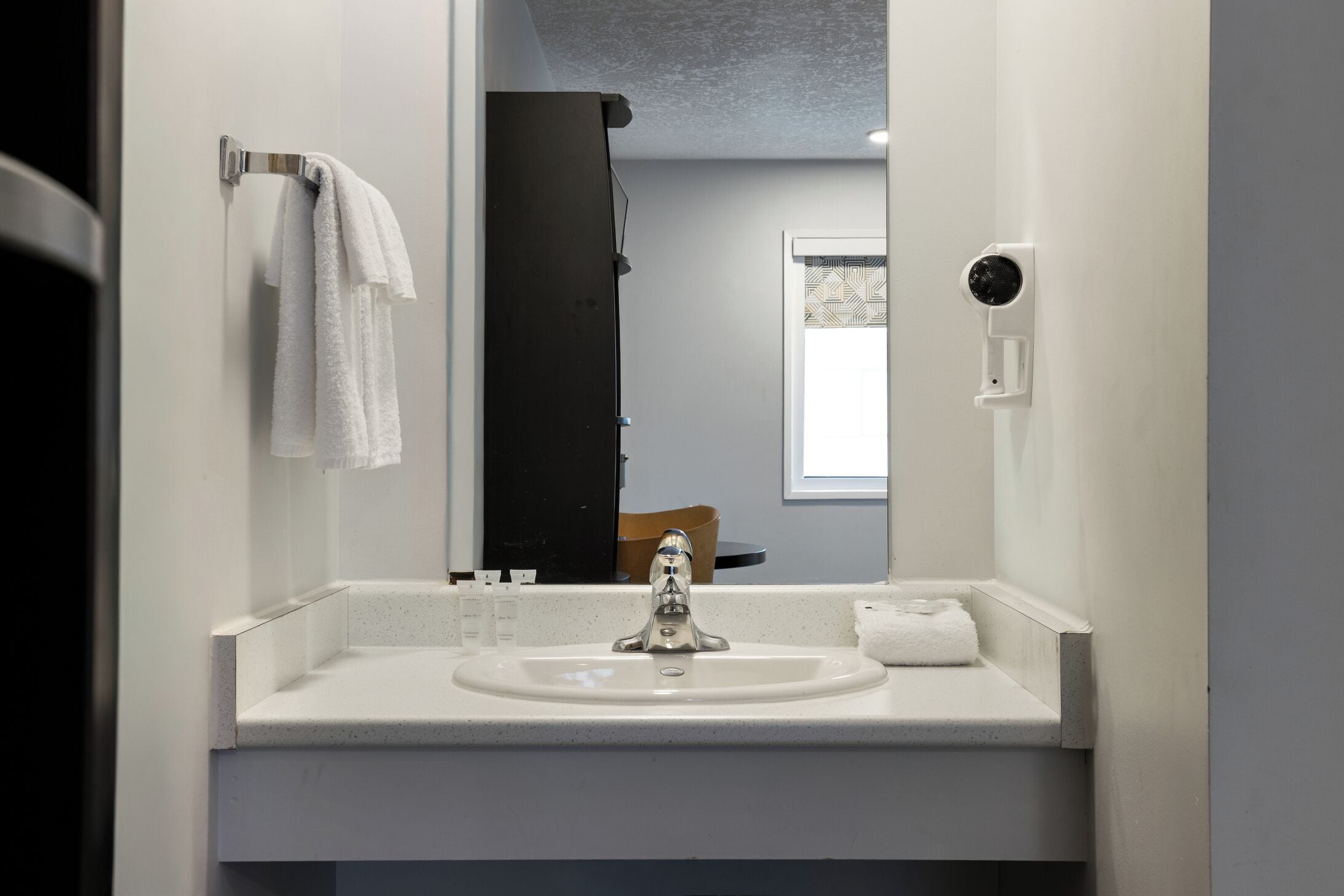 A bathroom with a white sink, a towel rack, and a mirror reflecting a shower area.