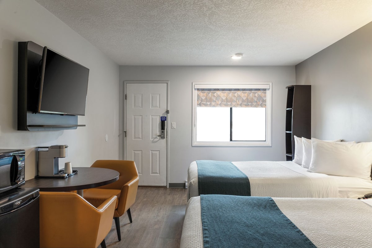 A hotel room with a bed, a desk with a coffee maker, a TV, and a window with patterned curtains.