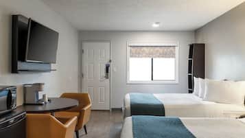 A hotel room with a bed, a desk with a coffee maker, a TV, and a window with patterned curtains.