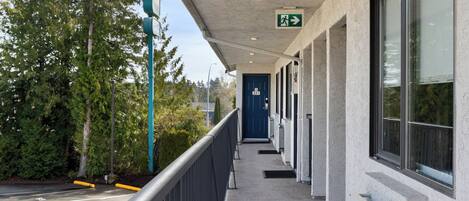 A building exterior with a covered walkway, a blue door, and a green emergency exit sign.
