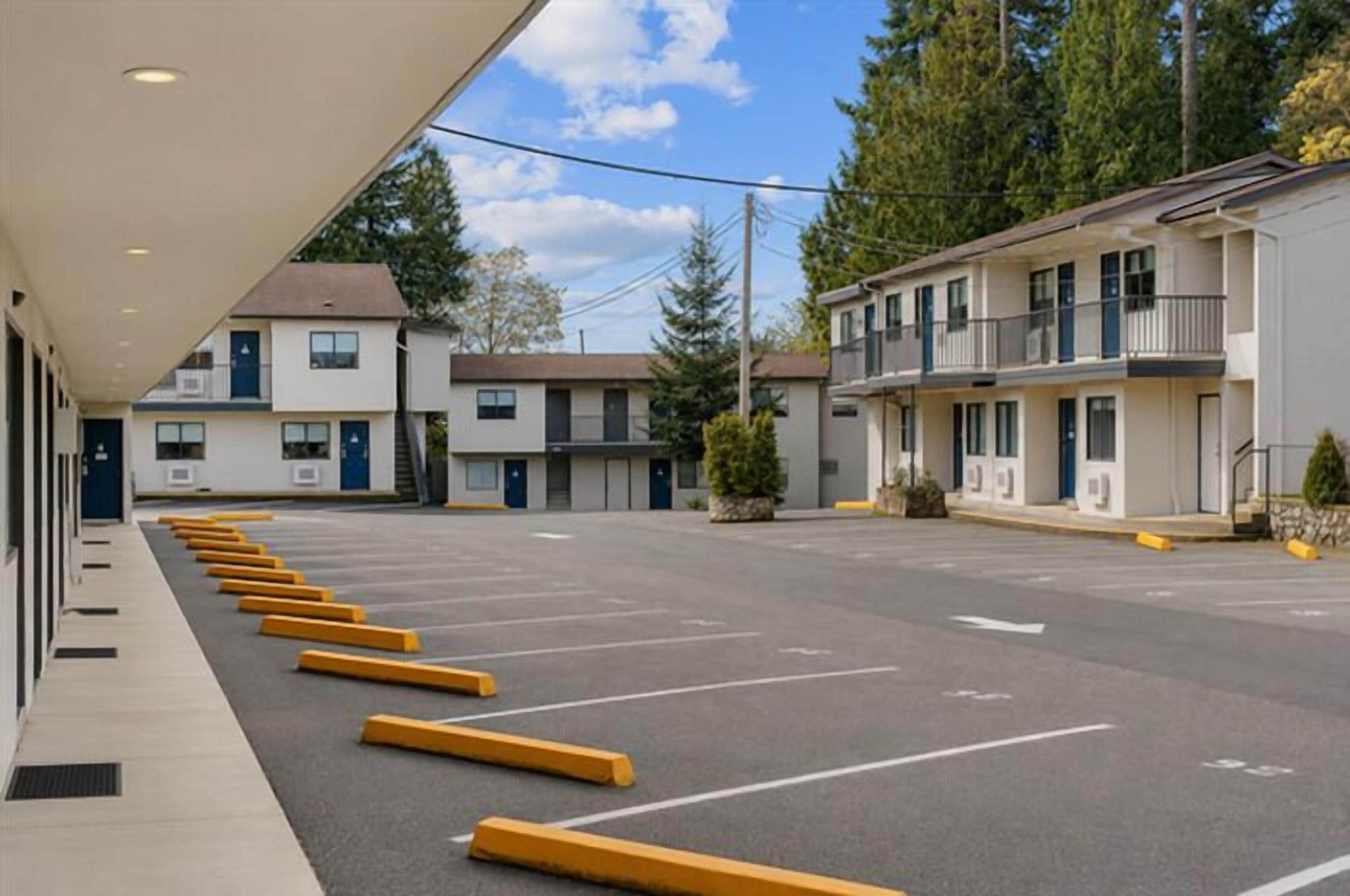 A motel with a row of parking spaces, a covered walkway, and a building with multiple floors and balconies.