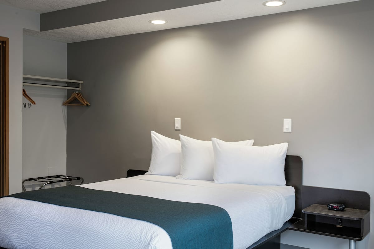 A hotel room with a bed, bedside table, and a coat rack.