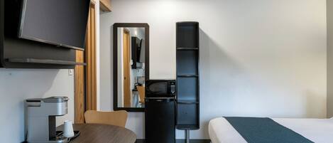 A hotel room with a bed, a desk with a coffee machine, a microwave, a mirror, and a TV.