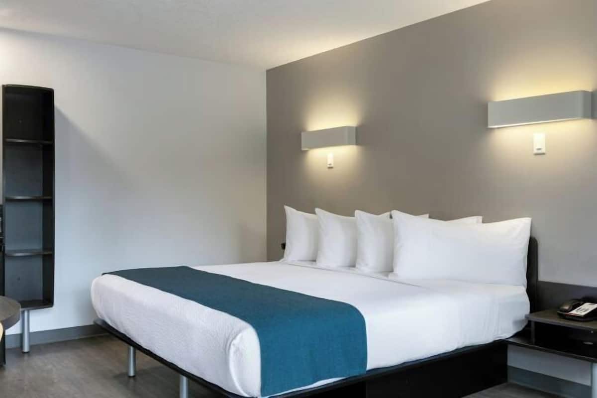 A hotel room with a bed, bedside tables, a nightstand, and wall-mounted lighting.