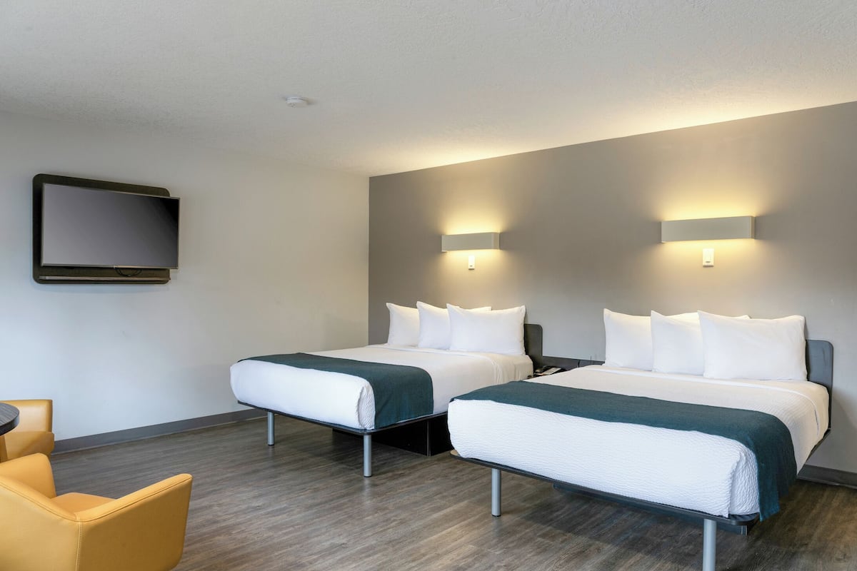 A hotel room with two beds, a flat-screen TV, a desk, and a chair.