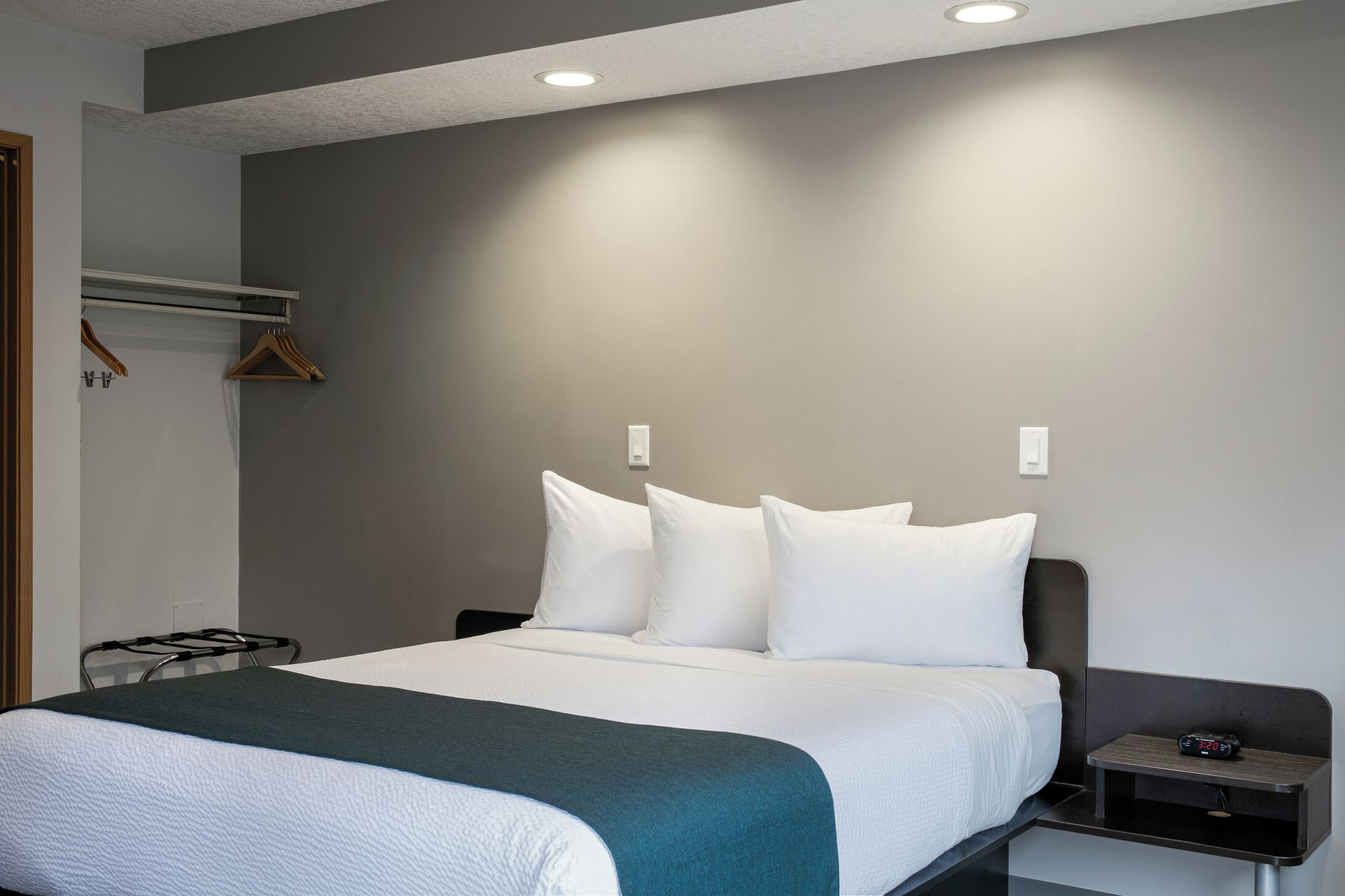A hotel room with a bed, bedside table, and a wall-mounted coat rack.