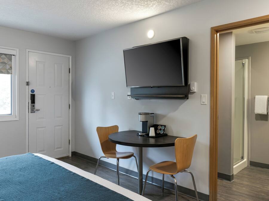 A hotel room with a bed, a coffee maker, two chairs, a TV, and a door.