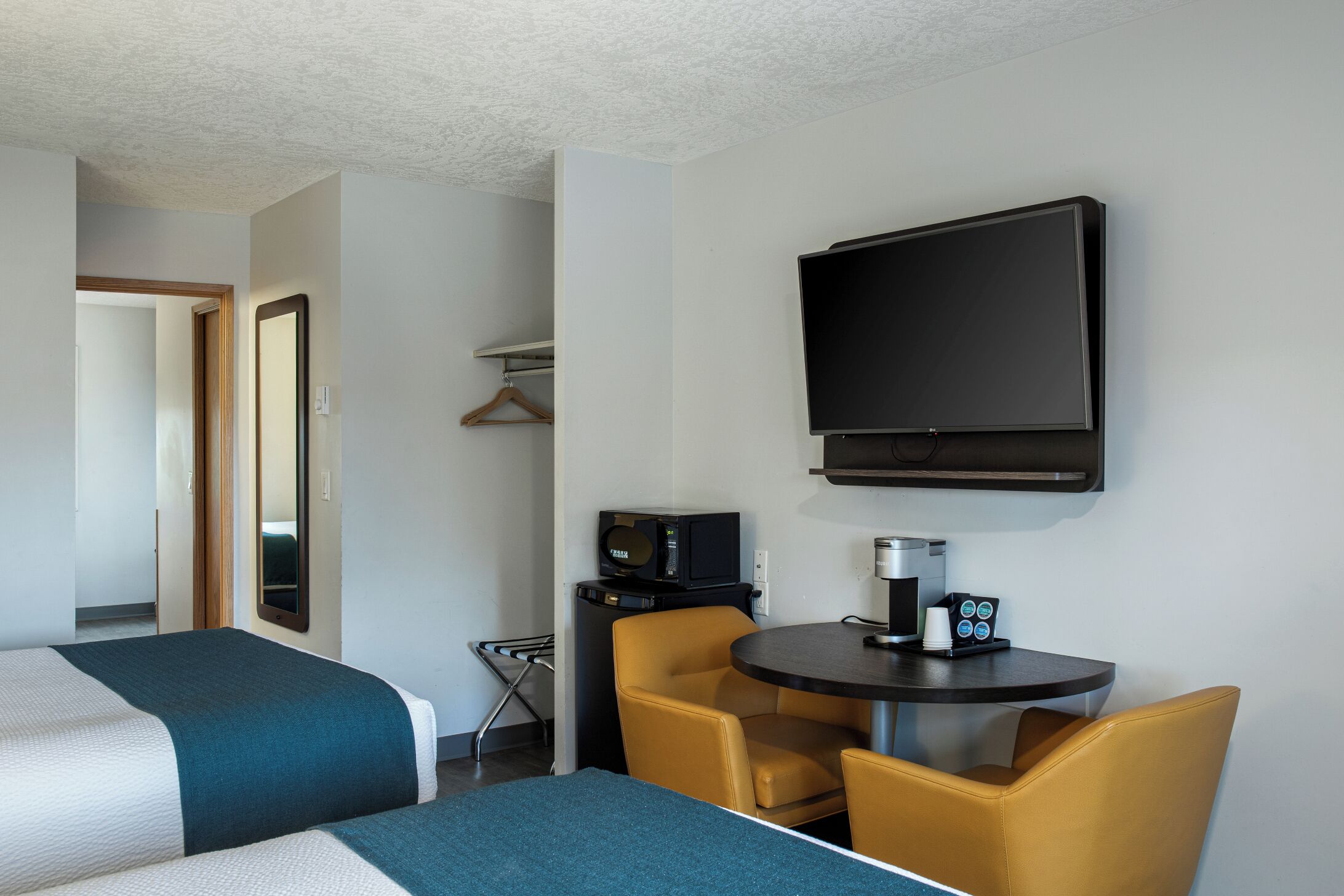 A hotel room with two beds, a TV, a coffee machine, and a small table with chairs.