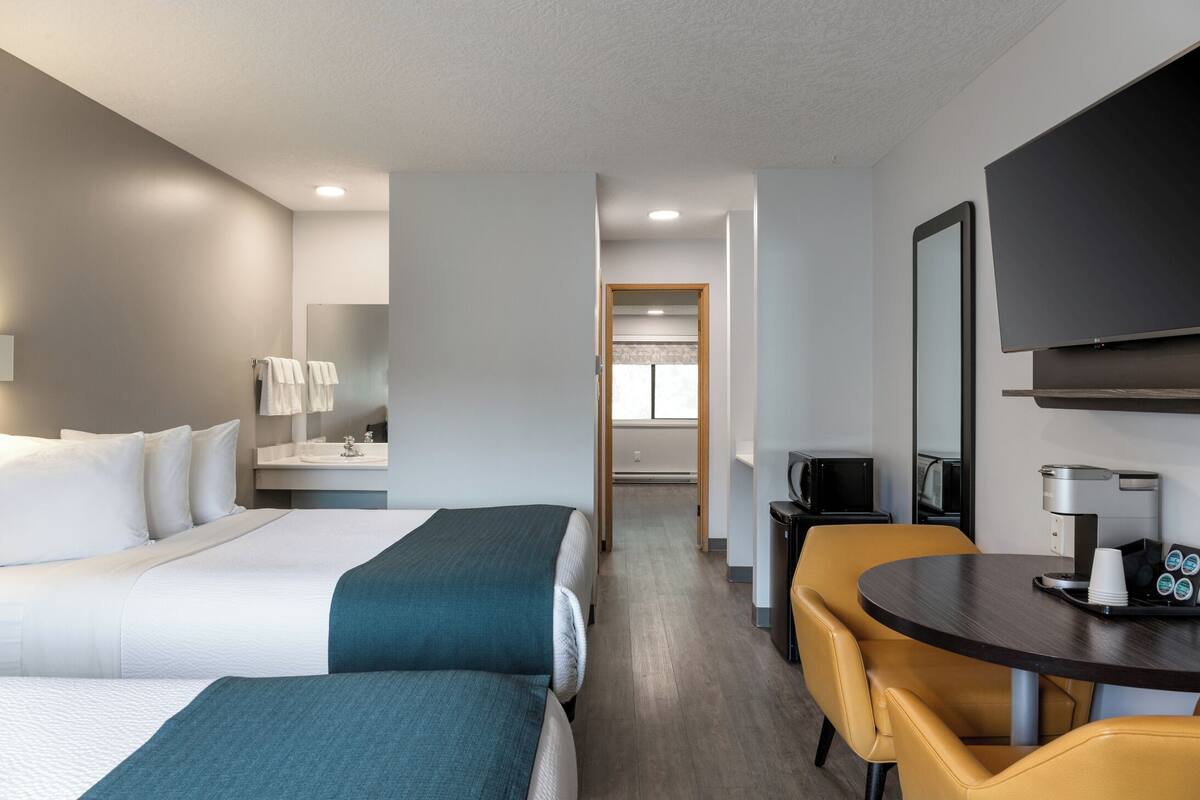 Une chambre d’hôtel avec deux lits, un bureau, une chaise, un téléviseur à écran plat, une machine à café et un four à micro-ondes.