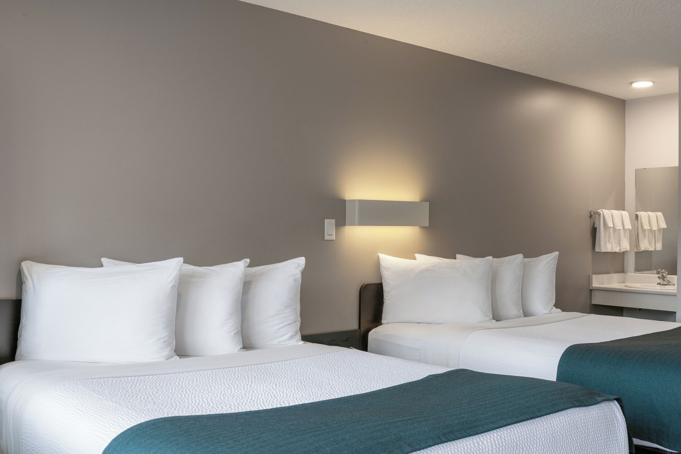 Une chambre d’hôtel avec deux lits, une table de chevet, un miroir et une lampe fixée au mur.