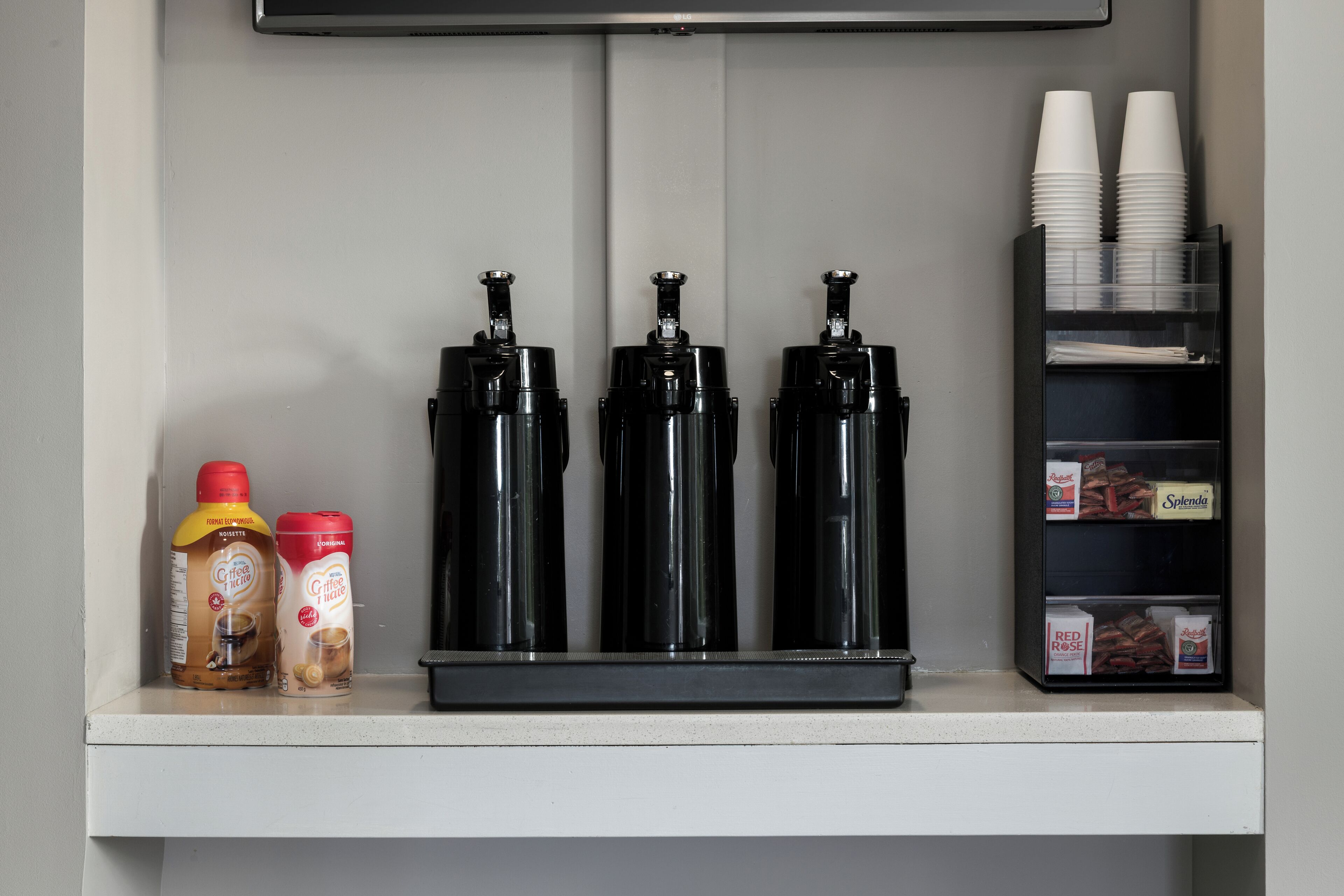 A beverage dispenser with coffee and tea options, a coffee grinder, and a cup holder with disposable cups.