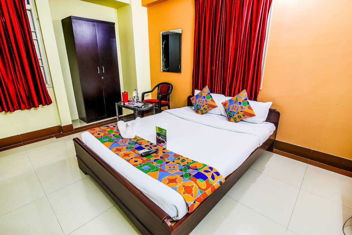 A hotel room with a bed, a chair, a small table, a wardrobe, and a mirror on the wall.