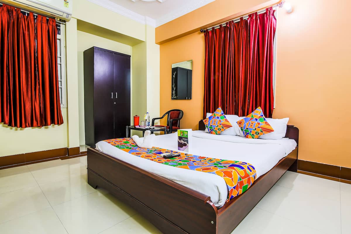 A hotel room with a bed, curtains, a wardrobe, a mirror, a chair, and a table with a remote control.