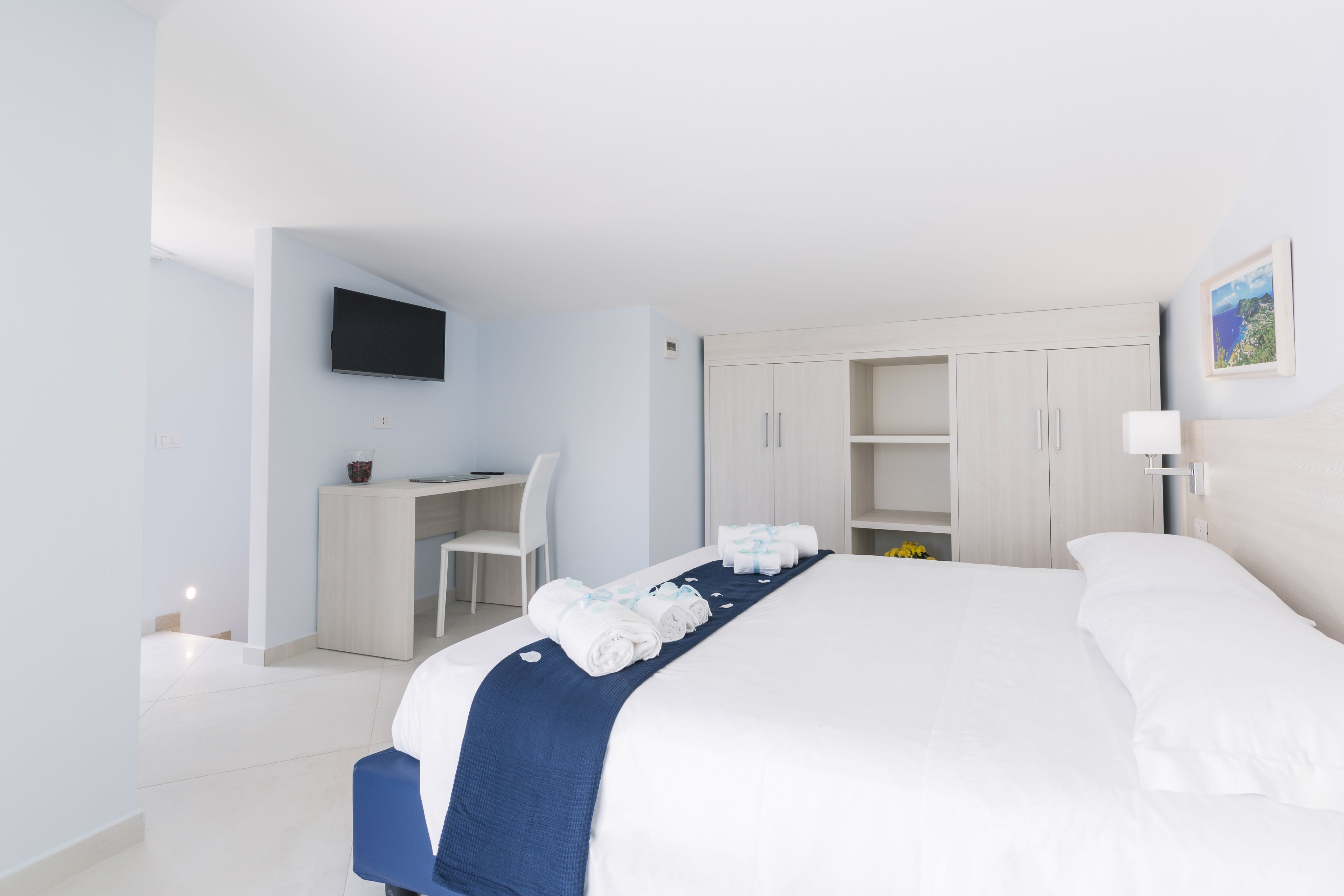 A modern hotel room with a large bed, a desk, and a TV mounted on the wall.