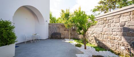 A courtyard with a stone wall, a small tree, a white planter, and a seating area with chairs.