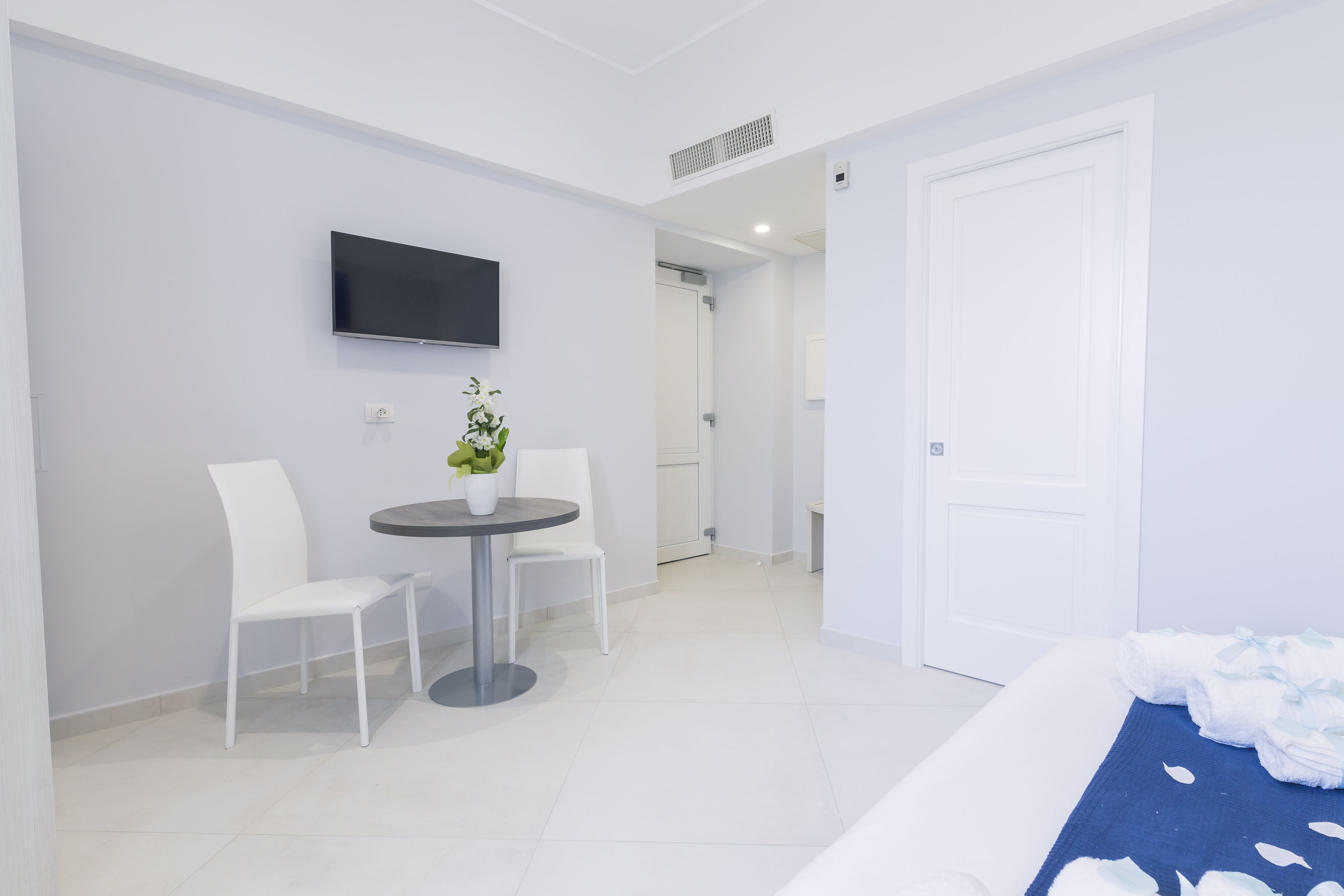 A hotel room with a bed, a TV mounted on the wall, a small round table with chairs, and a door leading to a bathroom.
