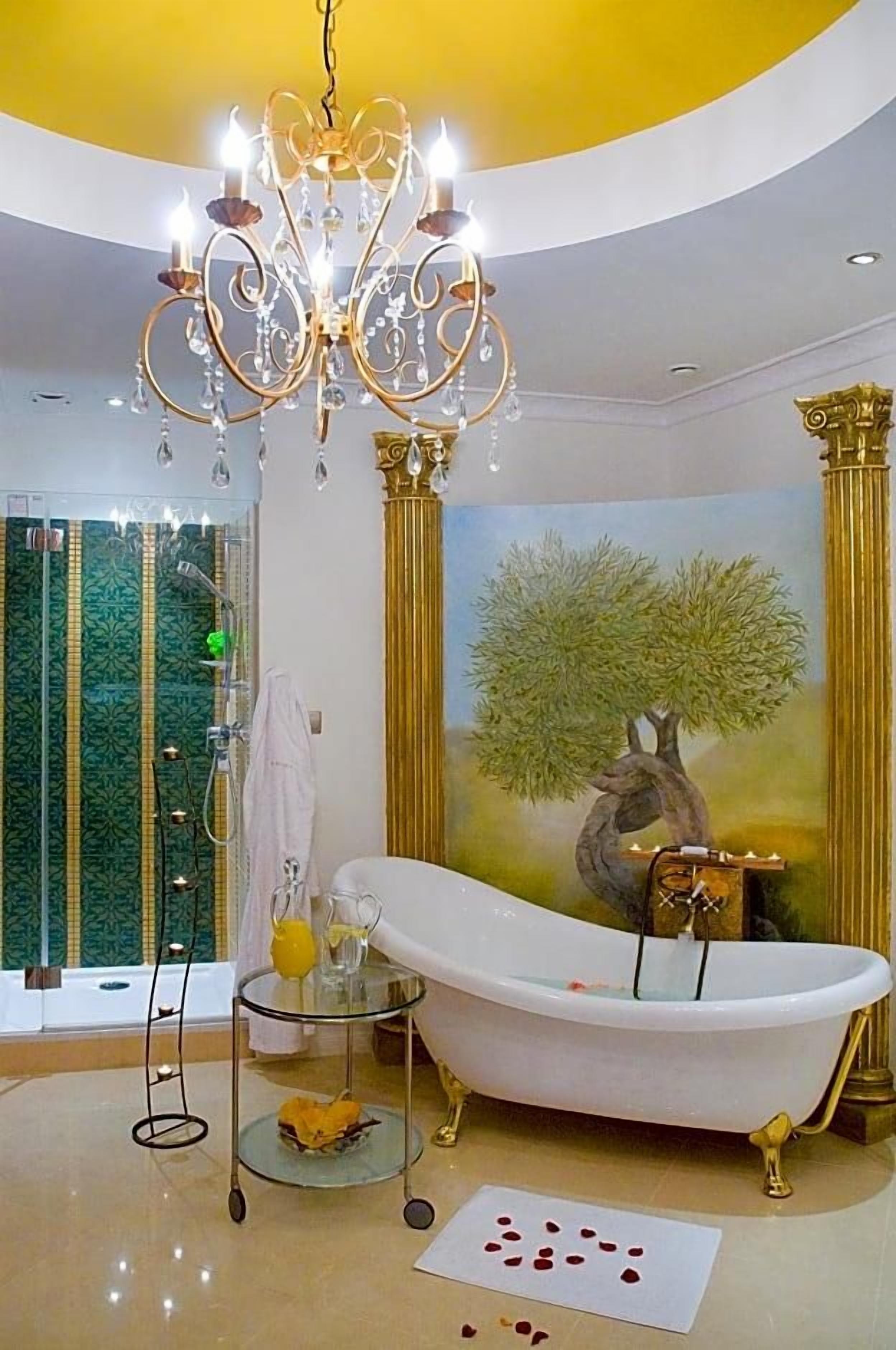 A luxurious bathroom with a freestanding bathtub, a chandelier, and a painting of a tree.