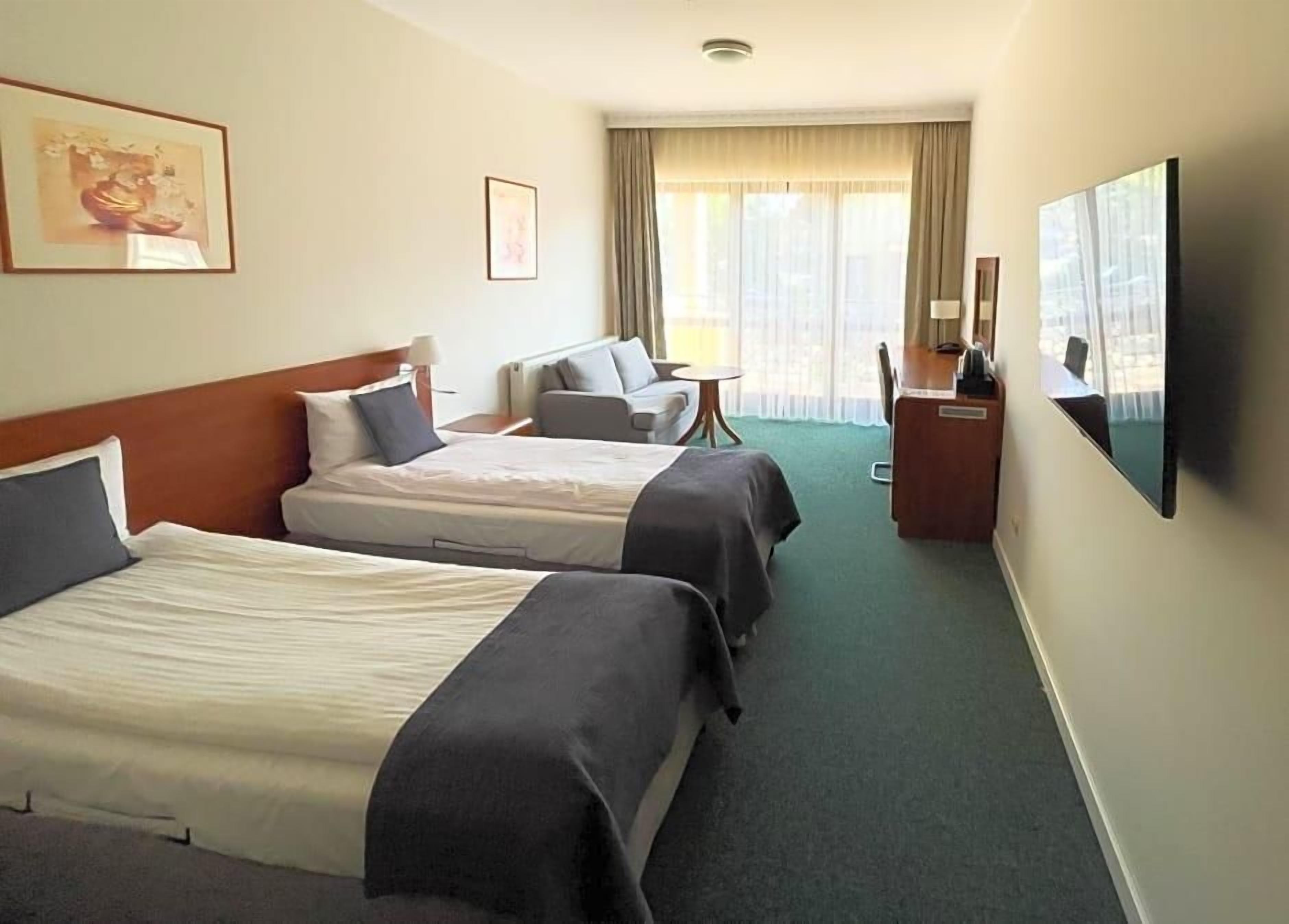 A hotel room with two beds, a sofa, a desk, and a television.