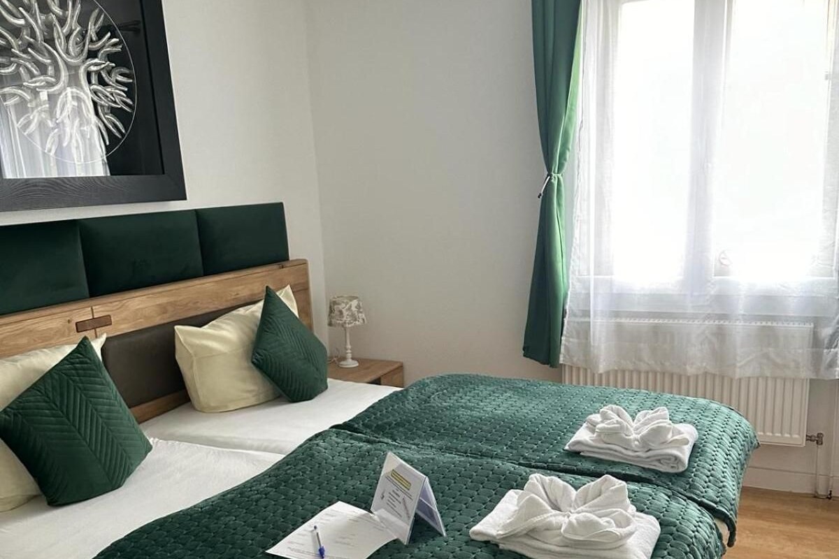 A neatly made double bed with green bedding, a headboard, and a bedside table with a lamp.