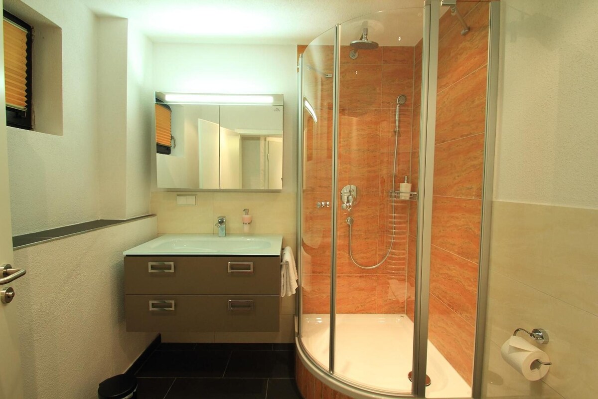 A bathroom with a glass-enclosed shower, a sink with a mirror above it, and a toilet.